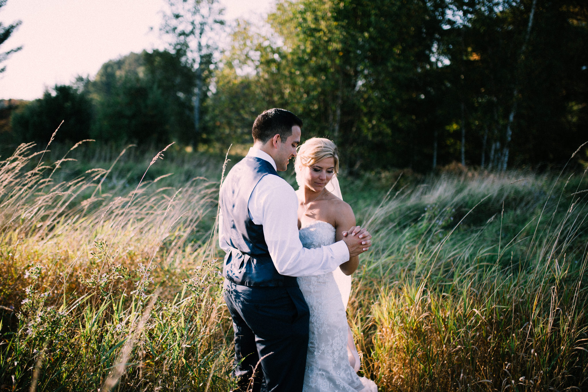 bride and groom holding hands in a field during sunset