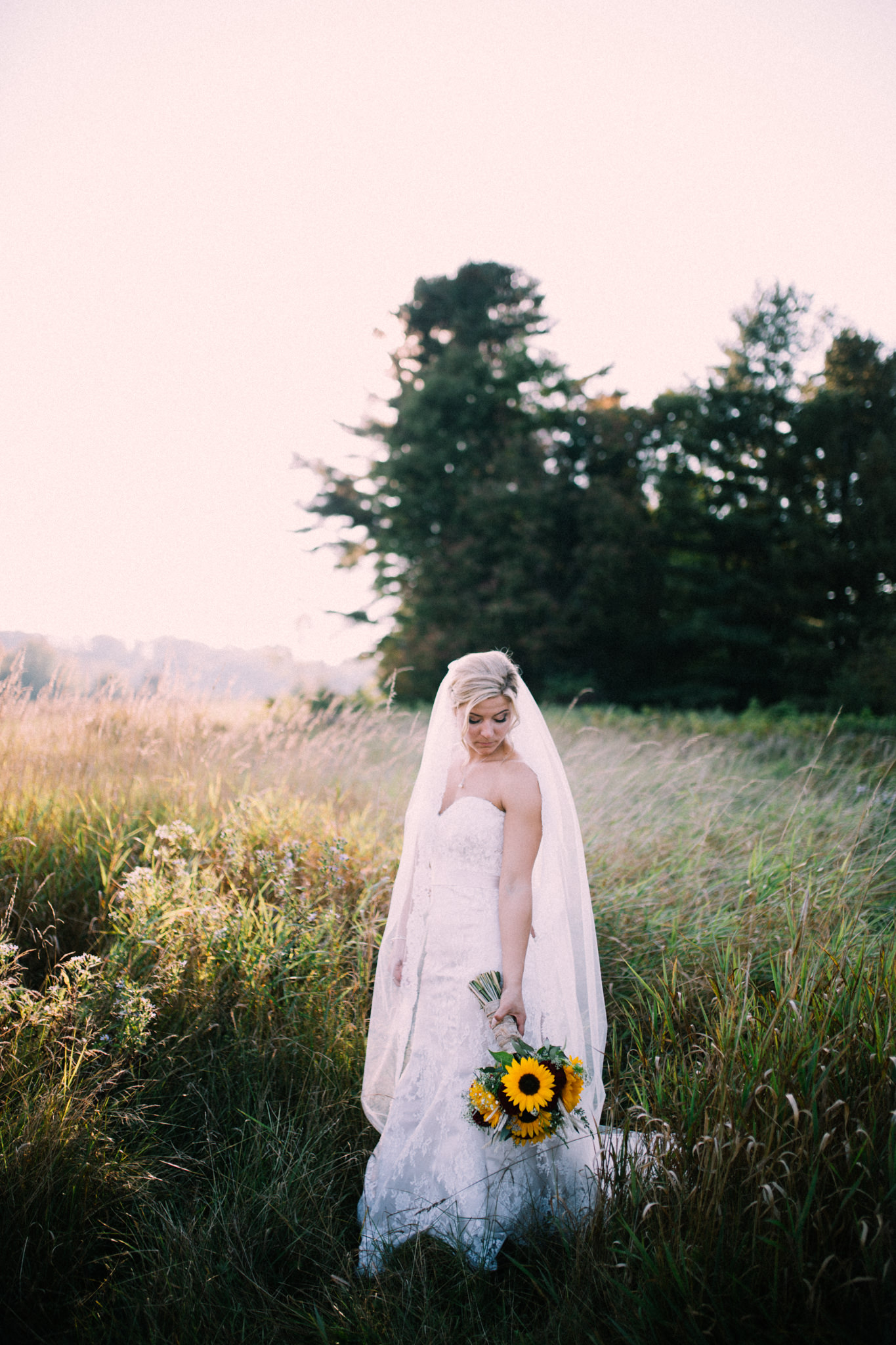 bride looking at her bouquet while standing in a field