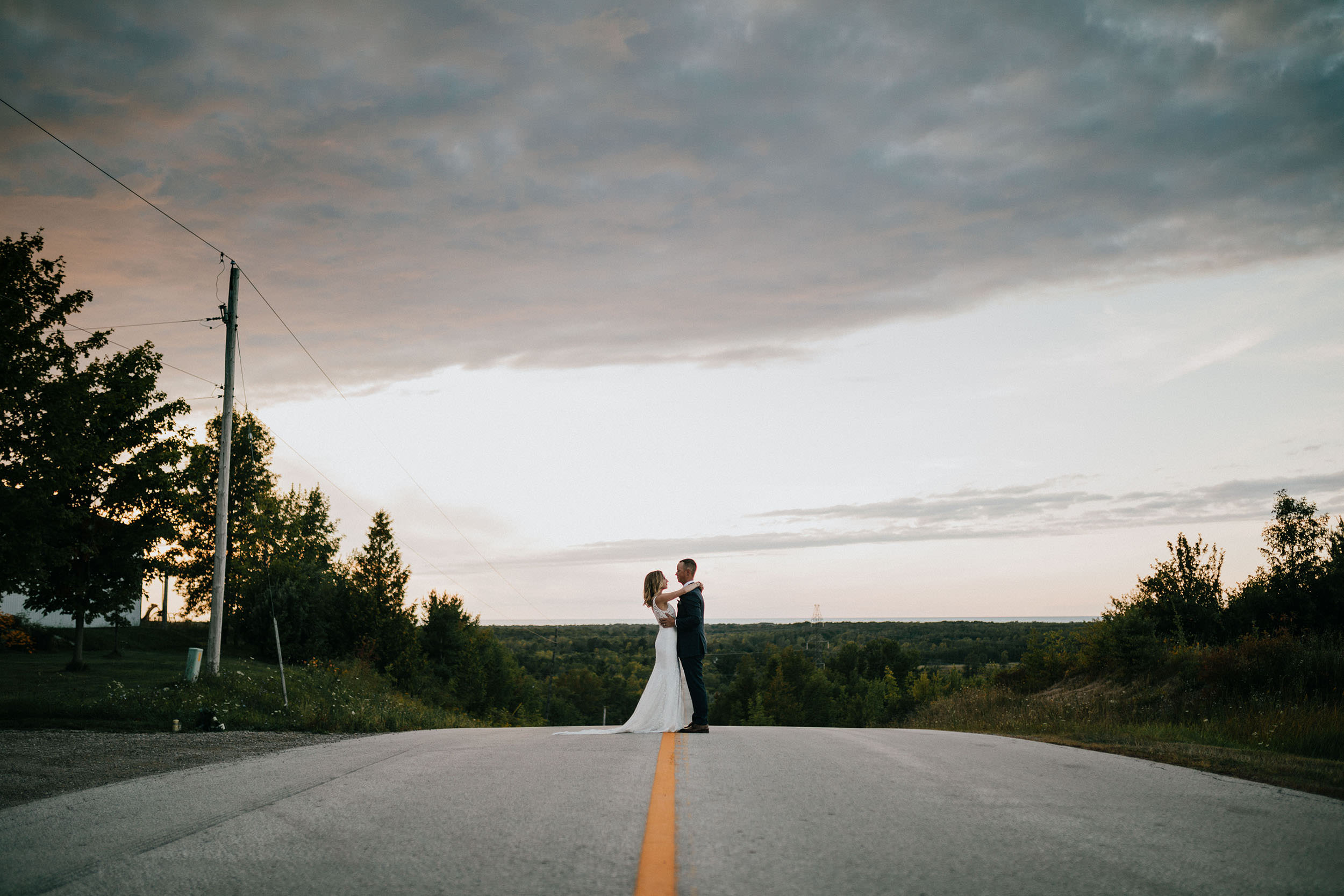 bride and groom embracing on road sunset